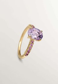 Anillo de oro con una gema ovalada de color púrpura claro, rodeada de pequeñas gemas rosas en una banda texturizada.