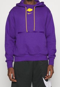 Sweat-shirt violet à capuche, cordons jaunes, poche zippée avant et logo. Fabriqué en matériau doux, avec une coupe décontractée et des poignets côtelés.