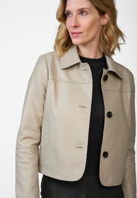 Beige leren jasje met een cropped ontwerp, knoopsluiting en twee voorkeepockets. Voorzien van een klassieke kraag en een soepele textuur.