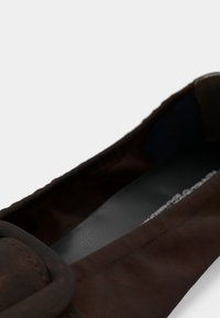 Ballerines en cuir marron avec un bout arrondi et un accent de large sangle. L'intérieur est doublé de noir lisse avec une semelle intérieure texturée.