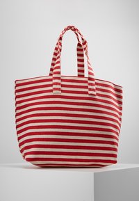 Sac fourre-tout rayé avec des rayures horizontales rouges et crème, fabriqué en tissu durable, doté de deux poignées robustes et d'un design spacieux.