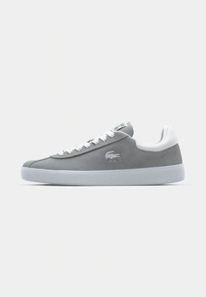 Gray suede sneaker with a white rubber sole and laces. Features a small logo and green accent on the tongue. Low-top design, smooth texture.