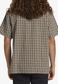 Chemise à manches courtes, à carreaux bruns avec des rayures verticales et des accents blancs, fabriquée en tissu léger et à coupe décontractée.