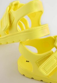 Gelbe Sandalen mit einem strukturierten Riemen, Klettverschluss und ausgeschnittenem Design für Atmungsaktivität. Die Sohle ist dick und hat ein Profil für Grip.