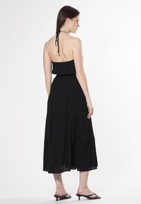 Schwarzes Maxikleid mit Neckholder, gerafftem Oberteil und schichteter Rock. Weicher Stoff, glatte Textur und knöchellanges Design.