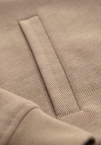 Beżowa tkanina o wyraźnej diagonalnej teksturze żebrowanej. Posiada kieszeń z czystym szwem wzdłuż krawędzi. Miękka, gładka powierzchnia.