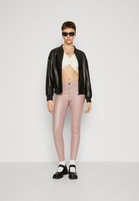 Svart lær bomberjakke, hvit cropped strikket topp, rosa tettsittende bukser, svarte platåskor og solbriller, med en dekorativ halskjede.