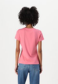 Kurzärmliges, pinkes Baumwoll-T-Shirt mit Rundhalsausschnitt und taillierter Form, kombiniert mit blauen Jeans. Sanfte Textur und einfaches Design.
