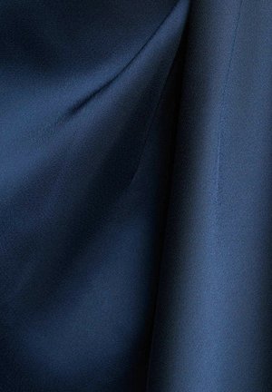 Primo piano di tessuto blu scuro liscio con pieghe morbide e cuciture sottili lungo un bordo.