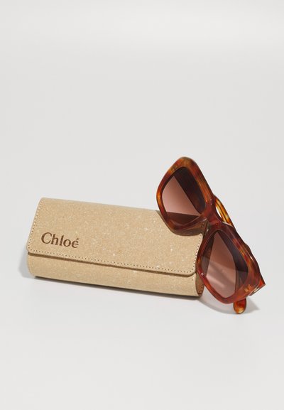 Lunettes de soleil en écaille de tortue avec des verres marron. L'étui est de couleur marron clair, texturé, et porte le logo "Chloé" en relief de couleur marron foncé.
