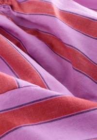 Roosa-punase triibulise mustriga kangas, millel on õhukesed mustad jooned. Tekstuur näib olevat kootud, nähtavad on pehmed voldid ja langev kangas.