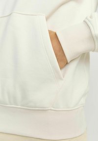 Sudadera de color crema con puños acanalados y bolsillo, de textura suave y sutiles detalles de costura.