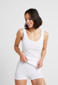Top in cotone bianco senza maniche con spalline larghe e scollatura a girocollo, abbinato a pantaloni corti bianchi aderenti; texture liscia senza motivi visibili.