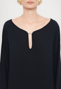 Ναυτική μπλούζα μακρυμάνικη με βαθύ V-λαιμόκοψη και ασημί λεπτομέρεια στην λαιμόκοψη. Φτιαγμένη από μαλακό, υφασμάτινο υλικό.