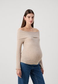 Beige ribbed off-shoulder maternity top with long sleeves and a draped neckline, paired with blue jeans. Smooth texture, form-fitting design.