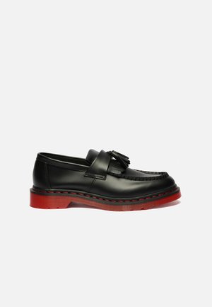 Mocassin à pampilles en cuir noir avec semelle épaisse rouge et surpiqûres rouges sur fond blanc.
