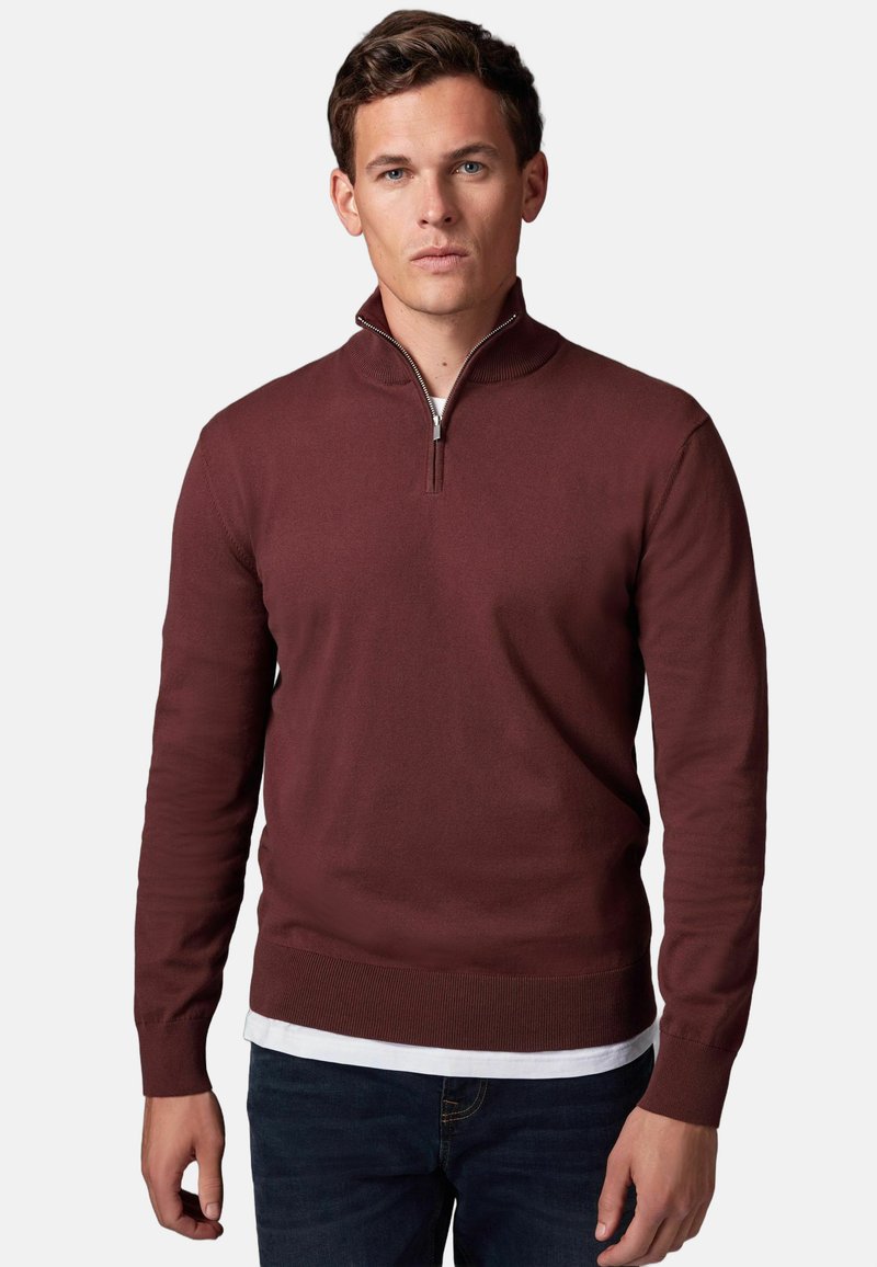 Bordeauxfarbener Pullover mit einem Viertelreißverschluss-Design, gerippten Bündchen und Saum. Aus leichtem Strickmaterial; über einem weißen Hemd getragen.