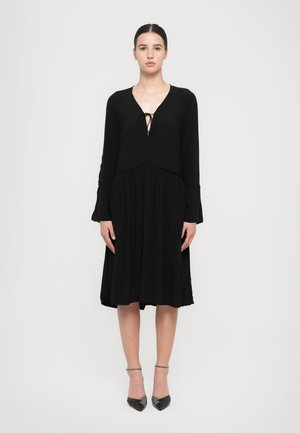 Black long-sleeve dress with a V-neckline and tie detail at the front. Flowy skirt and soft texture, reaching mid-calf.