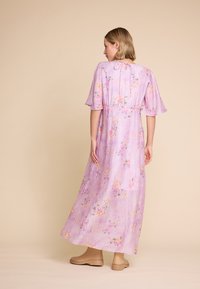 Lilla blomster maxi-kjole med korte flakete ermer, samlet bak, og et lett, teksturert stoff, parret med brune ankelboots.
