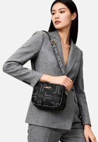 Borsa a tracolla nera con motivo geometrico, accessori dorati e finitura strutturata. Include una tracolla regolabile e un marchio evidente.