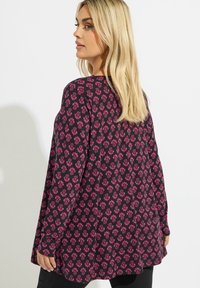 Top con motivo floreale su sfondo nero, caratterizzato da fiori rosa. Maniche lunghe e vestibilità comoda, con spacchi laterali per un comfort aggiuntivo.