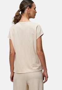 Top corto a maniche corte di un leggero color beige, con una vestibilità morbida. Tessuto morbido e texture, con un semplice scollo rotondo e bordi leggermente arrotolati.