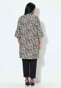 Tunika lunga con stampa leopardata nei colori beige, marrone e nero, con maniche a tre quarti, abbinata a pantaloni neri e tacchi a strappo.