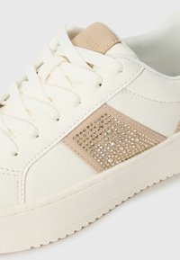 Hvide snørebånd sneakers med en syntetisk overdel, beige ruskindsdetaljer, tekstureret side og dekorative rhinsten. Gummisål.