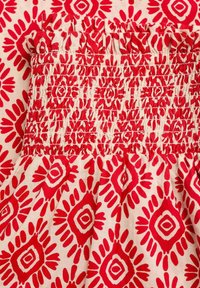 Tessuto a fantasia rosso e crema con un design a diamante e floreale. La fascia elastica arricciata in cima aggiunge texture e dimensione.