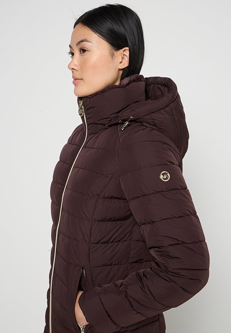 Veste matelassée bordeaux avec un design en quilt, capuche et accents en métal doré. Dispose de poches zippées et d'une silhouette ajustée.