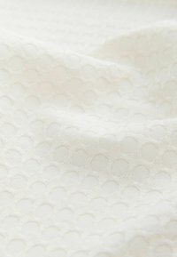 Tissu blanc avec un motif en nid d'abeille texturé, des plis doux et une apparence légèrement translucide.