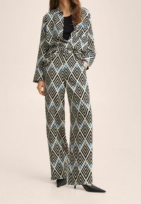 Camisa con estampado y pantalones de pierna ancha en negro, crema y azul. Diseño geométrico con un corte relajado y mangas largas. Zapatos de punta negros.