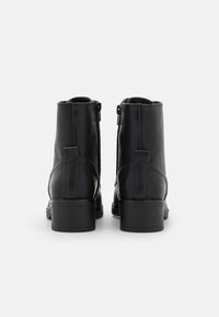 Bottes chevilles en cuir noir à texture lisse, fermeture éclair de chaque côté et talon bloc solide. Design minimaliste avec bout arrondi.