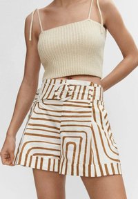 Top corto beige a costine con spalline sottili abbinato a pantaloni corti bianchi con motivi astratti a strisce marroni e una cintura con fibbia rotonda.