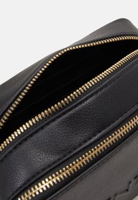 Sac en cuir noir avec des zips dorés, présentant une surface texturée et plusieurs compartiments pour l'organisation.