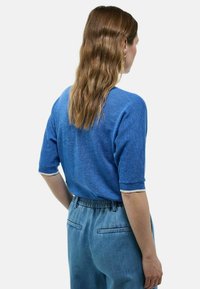 Gilet texturé bleu à manches courtes et bord blanc, associé à un pantalon taille haute bleu clair avec ceinture élastique et poches.