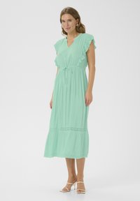 Vestido largo verde menta con mangas acampanadas, lazo ajustable en la cintura y detalles de encaje en el dobladillo de la falda. Tejido suave con un corte holgado.