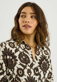 Camisa de botones floral en crema con patrones de cachemira en negro y marrón. Presenta un cuello y botones, fabricada en tejido ligero.