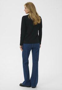 Un top negru cu mâneci lungi, asortat cu blugi evazați albaștri. Topul are o textură netedă, în timp ce blugii au un finisaj din denim și sunt croiți lejer.