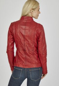 Rote Lederjacke mit figurbetontem Design, vertikalen Nähten und Stehkragen. Über dunkler Denim mit Taschendetails getragen.