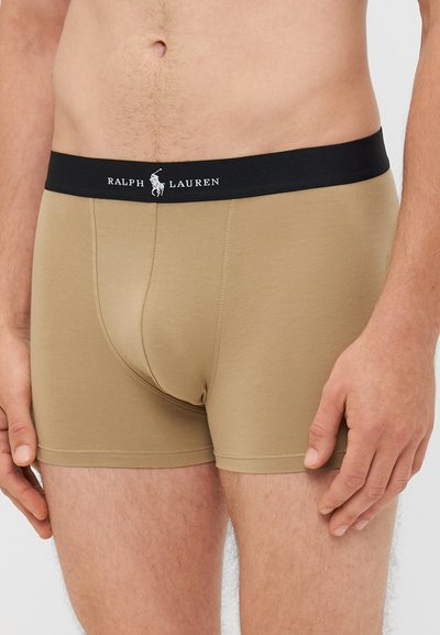 Bež boxer kratke hlače z črnim elastičnim pasom, na katerem je napis "RALPH LAUREN"; gladka tekstura in prilegan obliko.