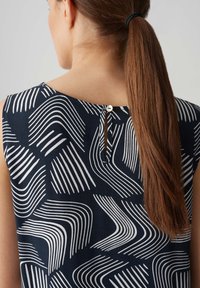 Navy ärmellose Bluse mit weißem Wellenmuster, ausgestattet mit einer Keyhole-Rückenöffnung, die mit einem Knopf gesichert ist. Glatte Textur und lockere Passform.