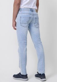 Vaqueros de denim azul claro con corte ajustado, que cuentan con bolsillos laterales y traseros, detalles de costura y una etiqueta con el logo en la cintura.