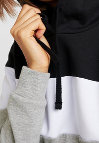 Hoodie med svarta, vita och grå färgblock; blandad bomullstextil; har justerbar dragsko och ribbade ärmslut.