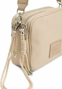 Beige schoudertas van textuurcanvas, met dubbele ritscompartimenten, zilverkleurige hardware en decoratieve touwaccenten met groene punten.