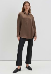 Bruine satijnen lange mouw blouse met een knoopsluiting aan de voorkant, gecombineerd met zwarte strakke broek en zwarte instappers. Minimalistisch ontwerp.