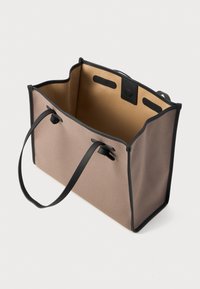 Stor totebag i lys brun tekstil med svarte lærdetaljer. Har lange håndtak og en åpen toppdesign, med romslig innvendig plass.
