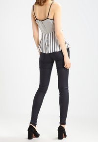 Top peplum de rayas en blanco y negro con tirantes y un diseño ajustado, combinado con pantalones negros ajustados y zapatos de tacón negros.