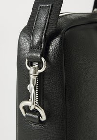 Schwarze Lederhandtasche mit strukturiertem Finish, ausgestattet mit einem silbernen Metallreißverschluss und Clipbeschlägen sowie einem gepolsterten Tragegurt für Komfort.