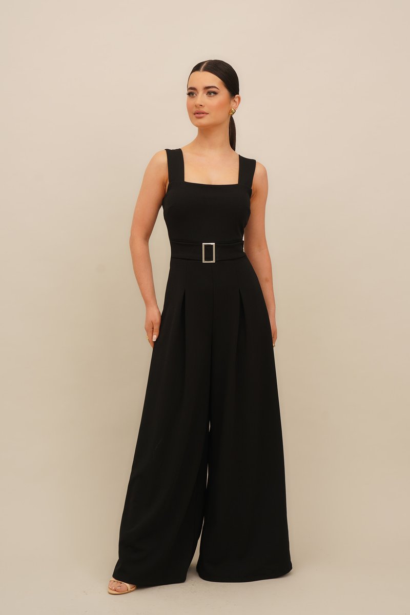 Melna kombinezons ar kvadrātveida kakla izgriezumu, platiem svārkiem un krokām. Iezīmēts ar definētu jostasvietu un taisnstūrveida jostas sprādzi.